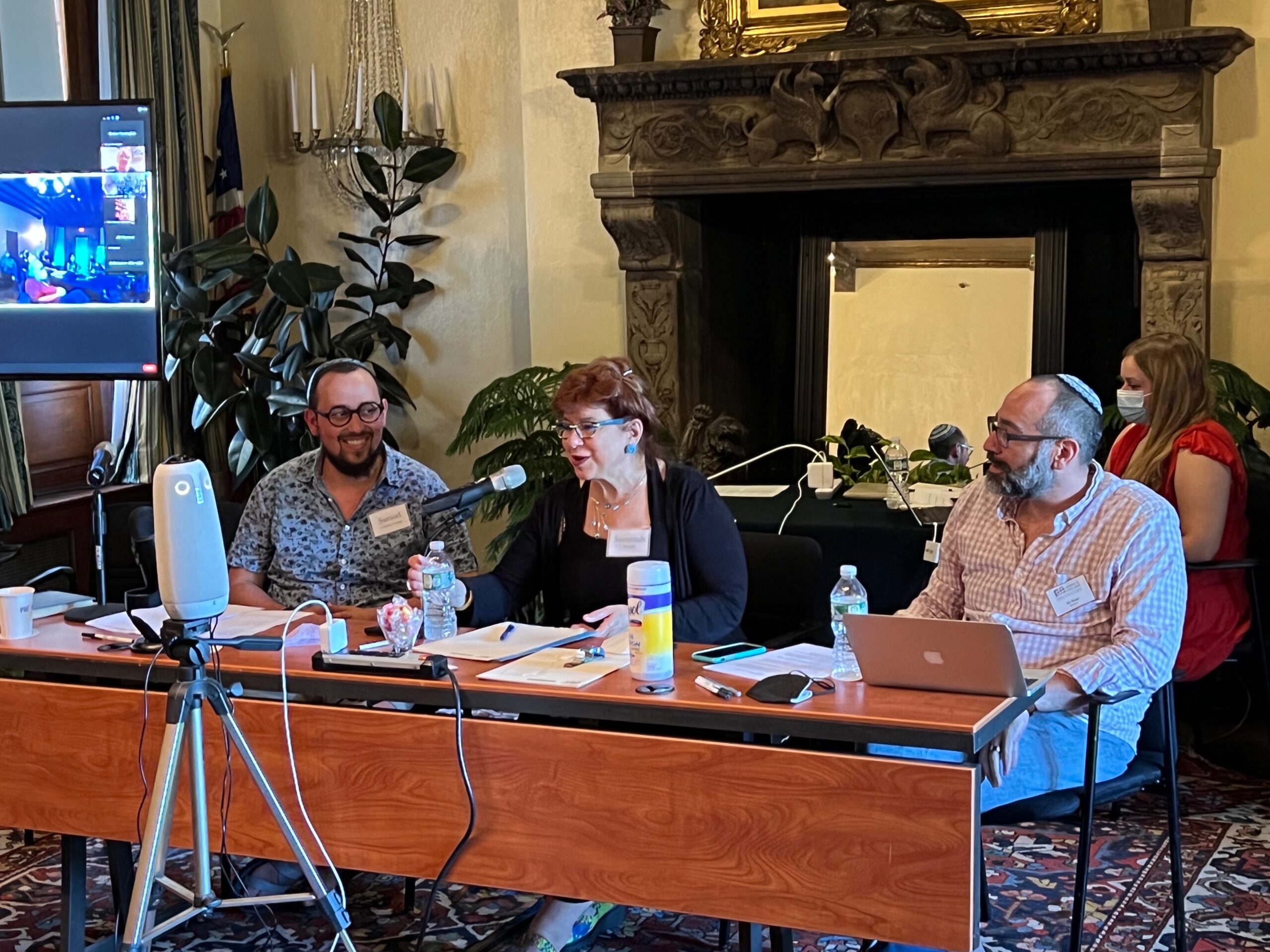 Three people sitting at a desk with a microphone pointed at the woman in the middle.