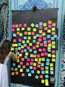 A board labeled "found" with a plethora of sticky notes attached to it. A woman is standing at the board, adding a new note.