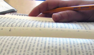 hand and pen resting on hebrew book