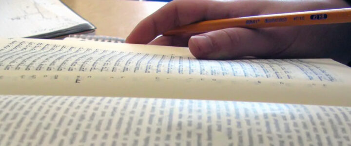 hand and pen resting on hebrew book
