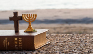 cross and menorah on a bible by the beach