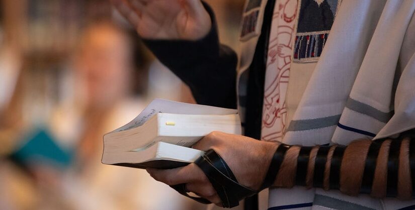 Arm wrapped in tefillin holding a prayerbook