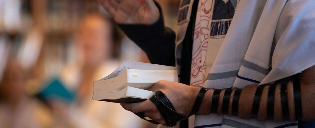 Arm wrapped in tefillin holding a prayerbook